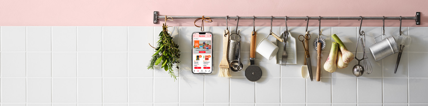 På en stång med köksredskap i ett kök med rosa väggar och vitt kakel hänger en mobiltelefon med Hemköpappen öppen.