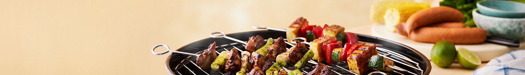 En rykande grill där det grillas grillspett med bitar av kött och färska grönsaker.