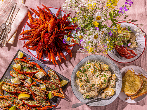 - [ ] Buffé med kräftor, blommor, potatissallad, gratinerade kräftstjärtar och bröd på en rosa bordsduk.